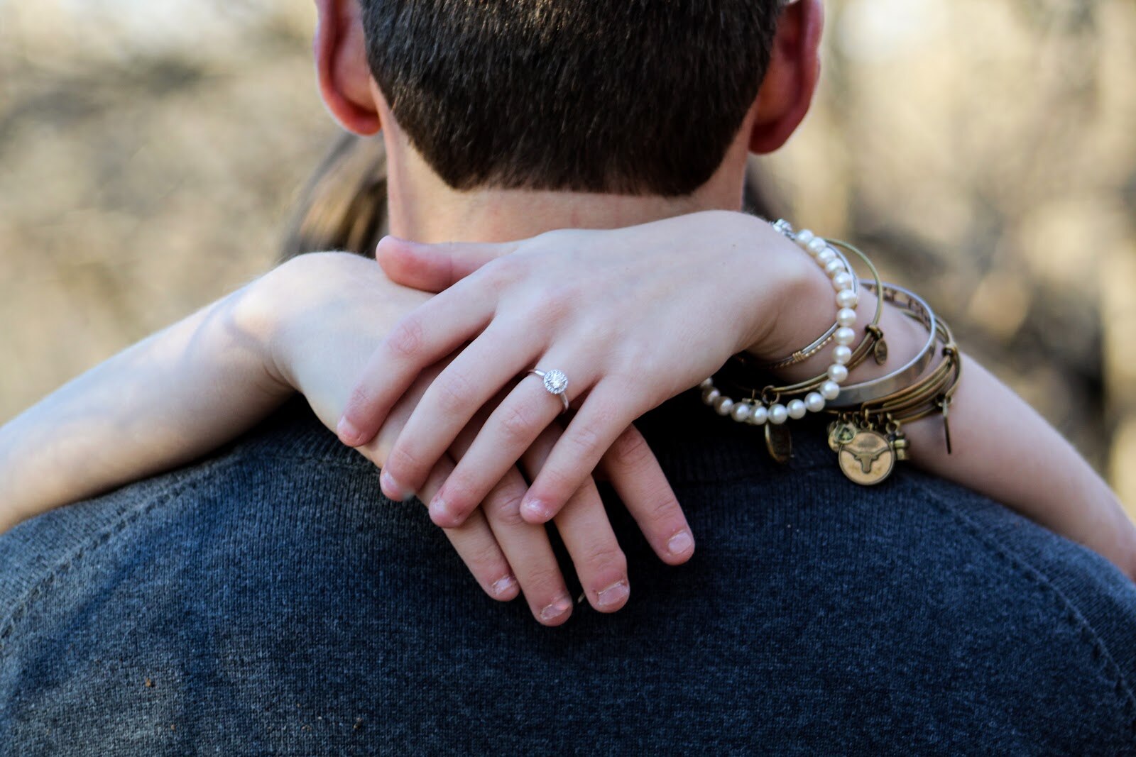 woman's hands around back of man's neck displaying engagement ring