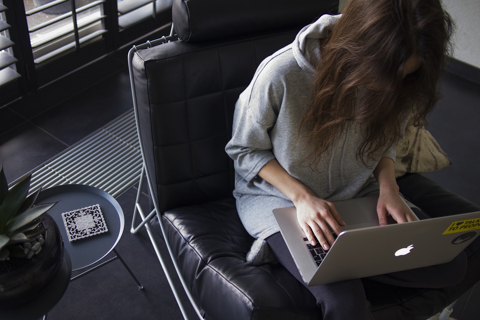 young woman in leather chair bent over laptop working